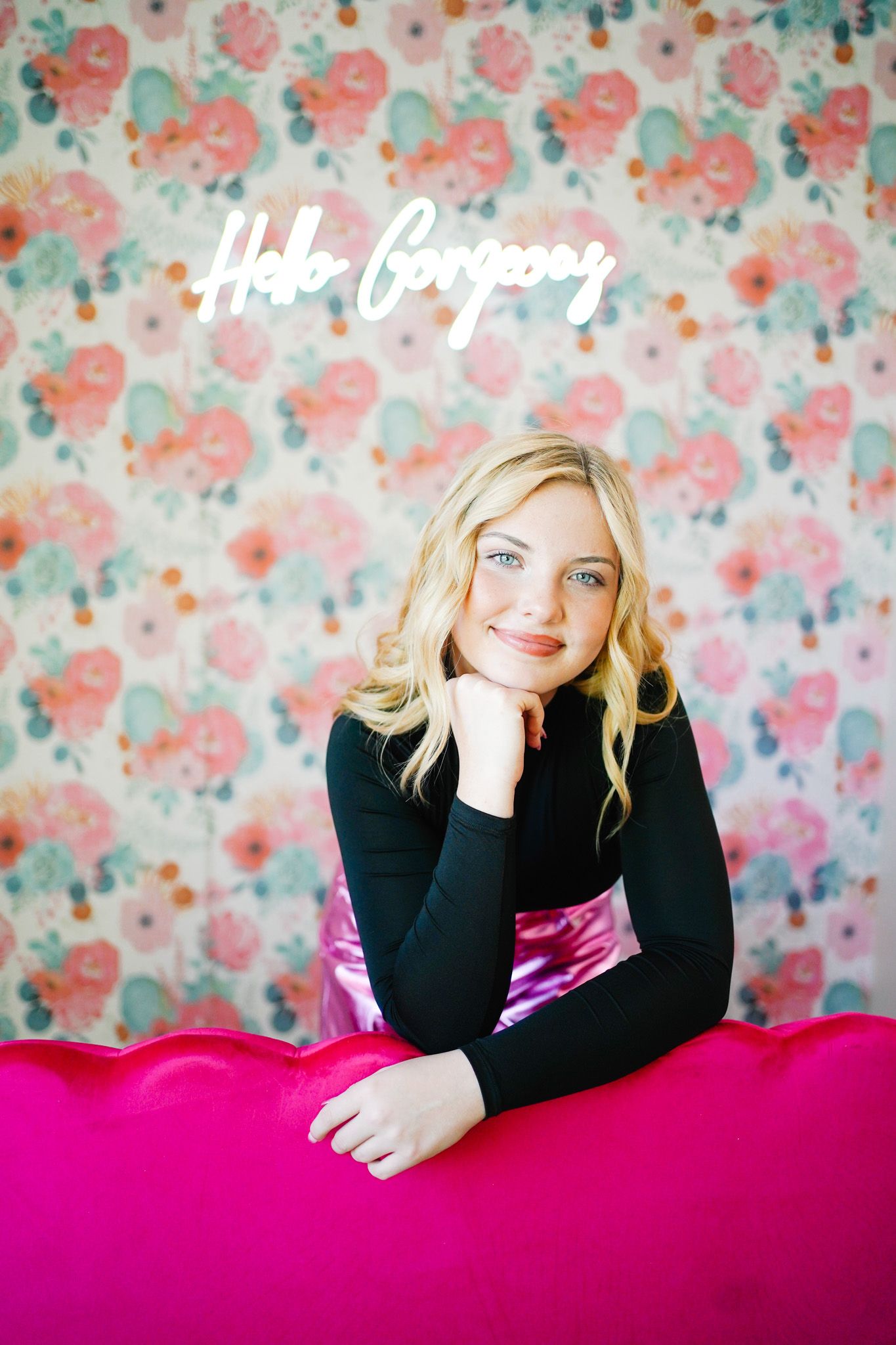 Portrait against floral wallpaper with bright pink accent and black sweater in modern setting.