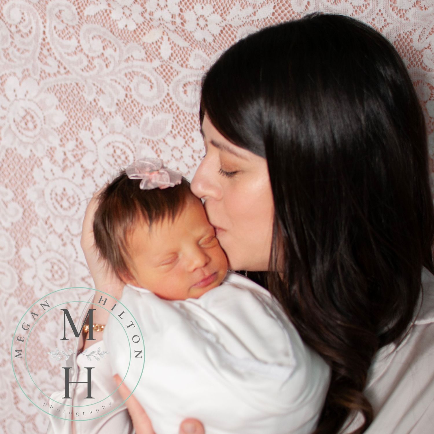 Mom kissing newborn baby girl candid photo against pink lace backdrop
