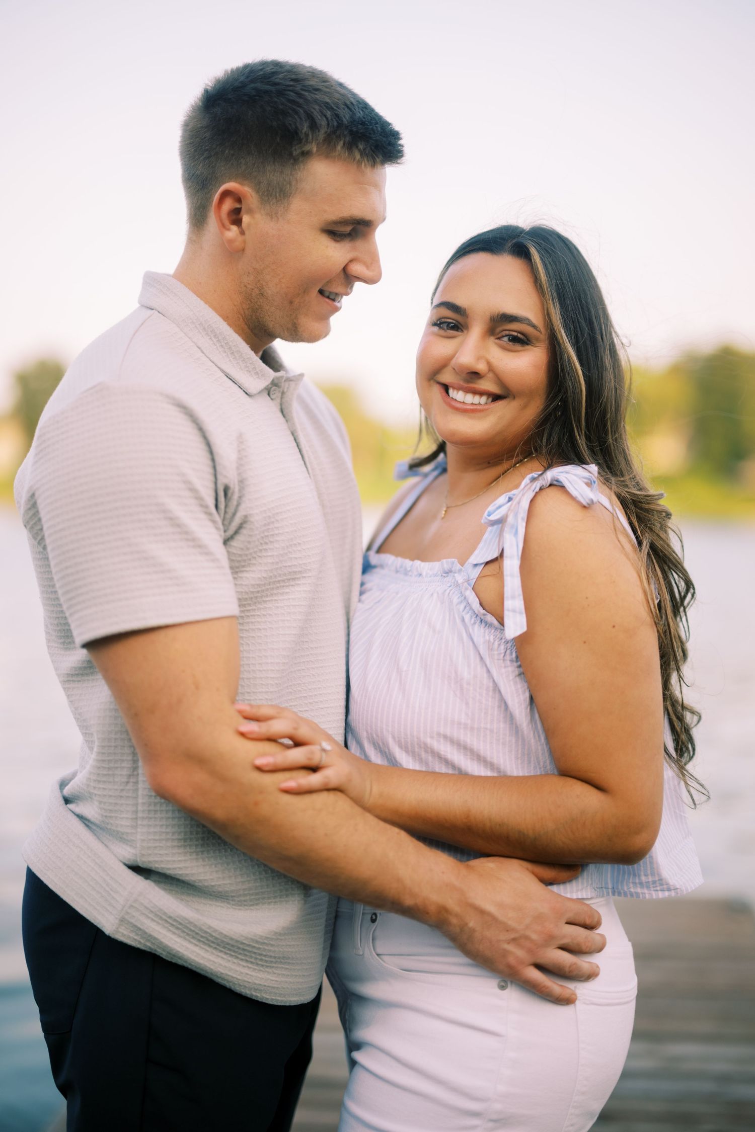 A couple embraces and smiles lovingly at each other while standing on a dock at sunset.