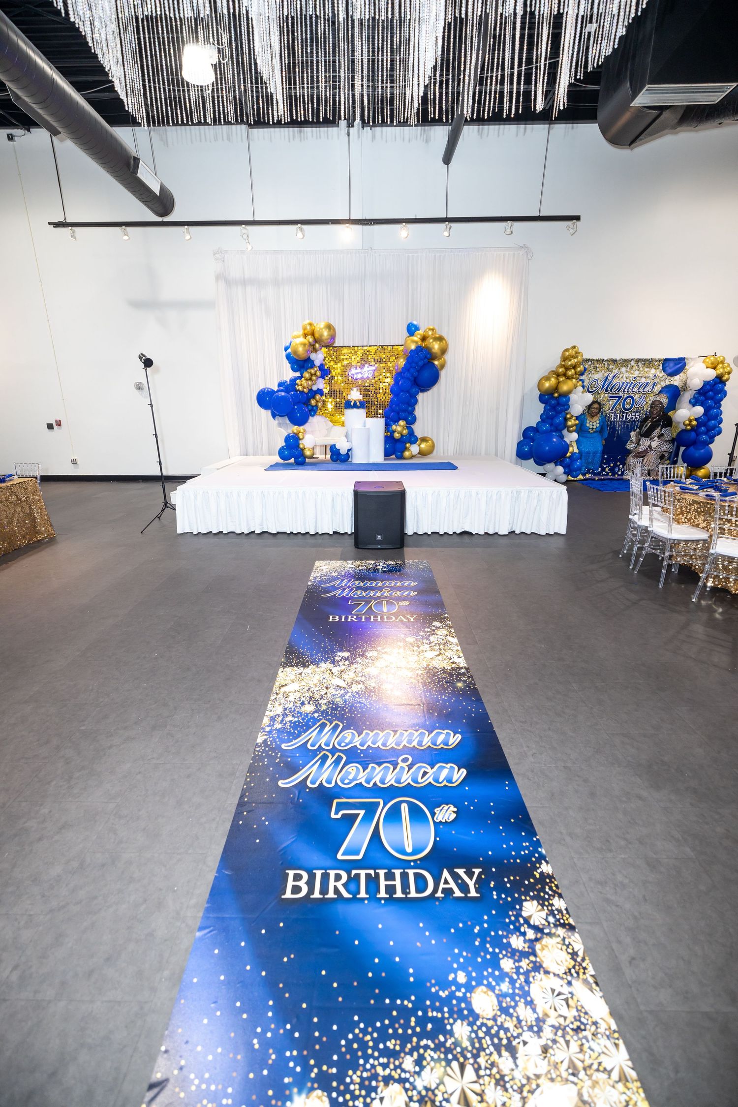 Event space setup with blue and gold balloon arch and custom birthday aisle runner.