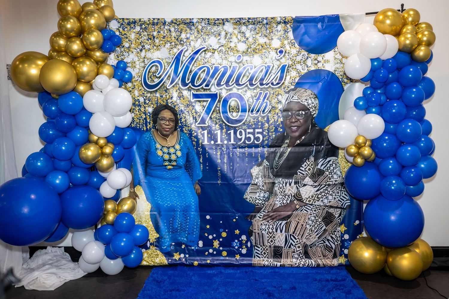 Party photo backdrop with Monica's logo, decorated with blue and gold balloon arrangements.