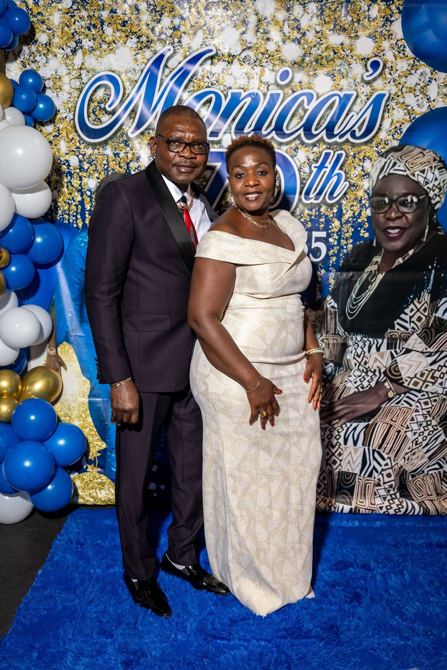 Elegant party setup with blue and gold balloon decor and cursive Monica's sign against a sparkly backdrop.