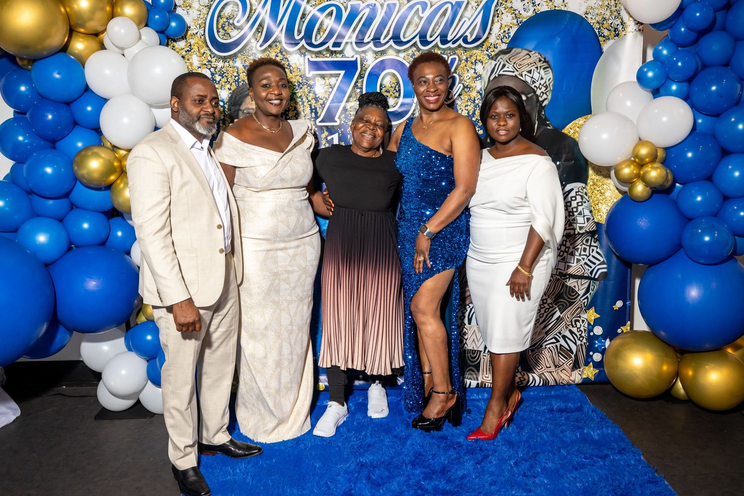 Group photo at formal event with blue and gold balloon decorations and elegant attire.
