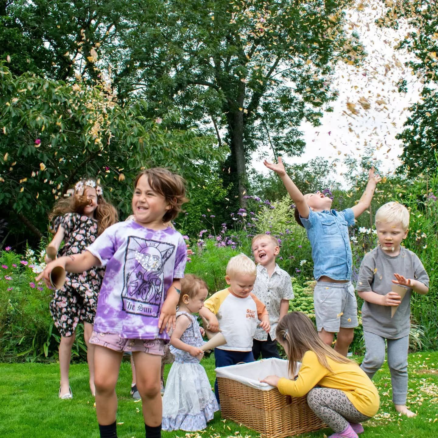 Joyful group of children celebrating a gender reveal with confetti in a lush garden.