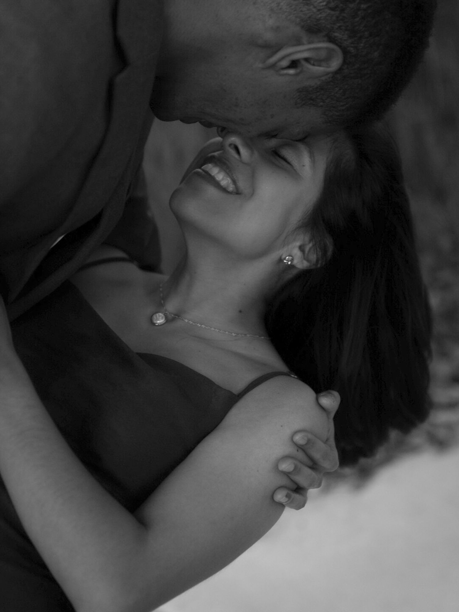 A joyful woman laughs as her partner kisses her forehead in a tender black and white portrait.