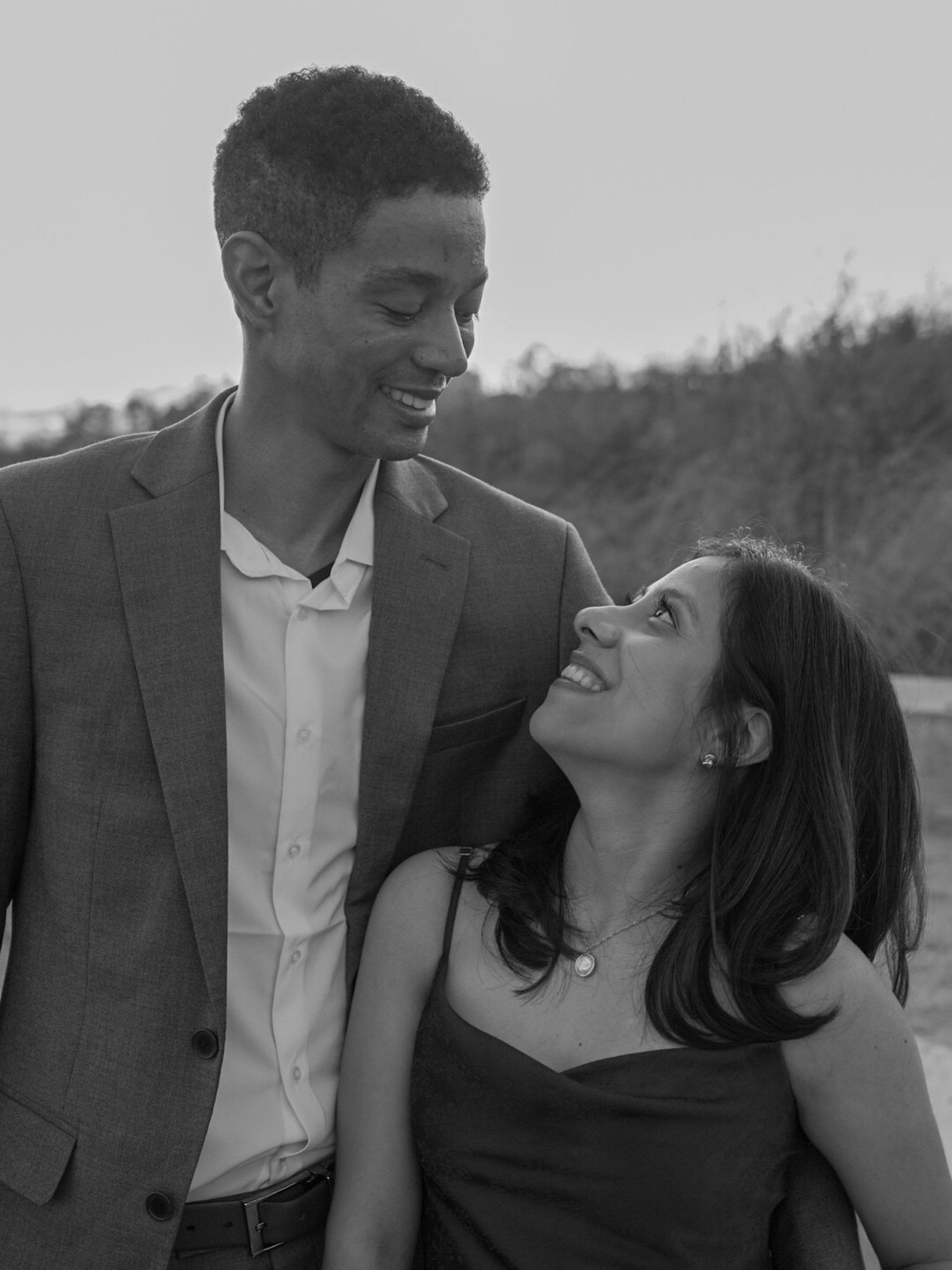 Black and white photo of a smiling couple gazing at each other outdoors.