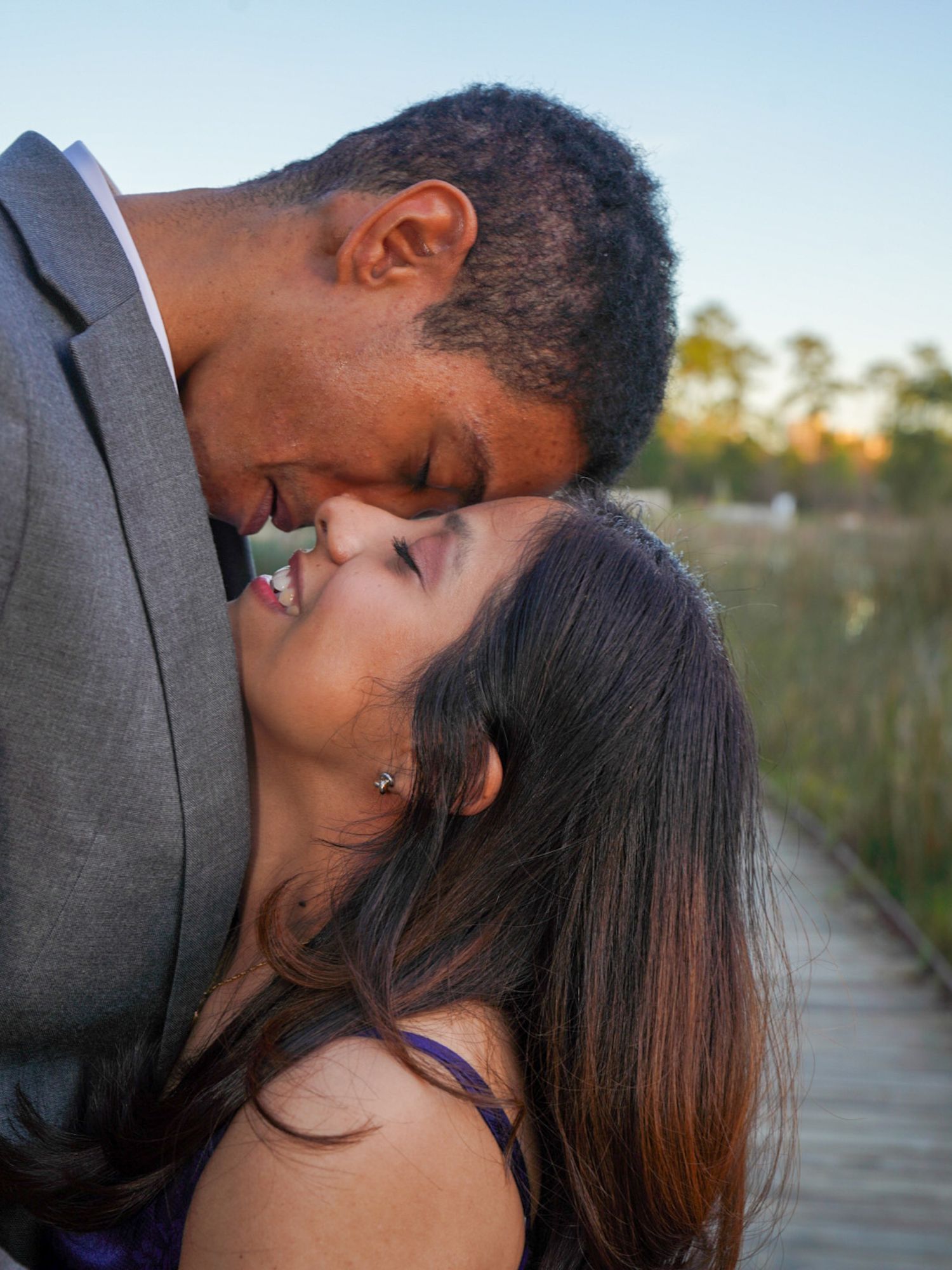 Romantic couple sharing a tender kiss on a wooden boardwalk at sunset.
