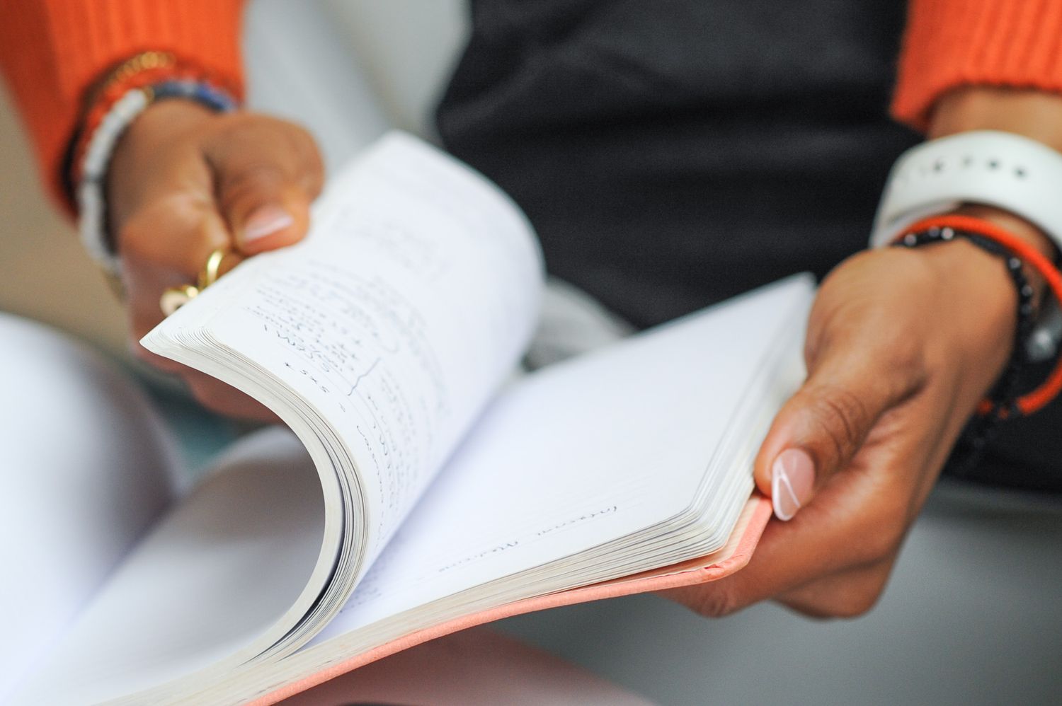 Person with bracelets reading an open book, turning pages with both hands.