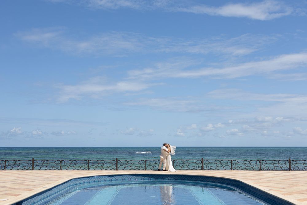 Couple embracing by ocean-view pool at a seaside wedding venue under blue skies.