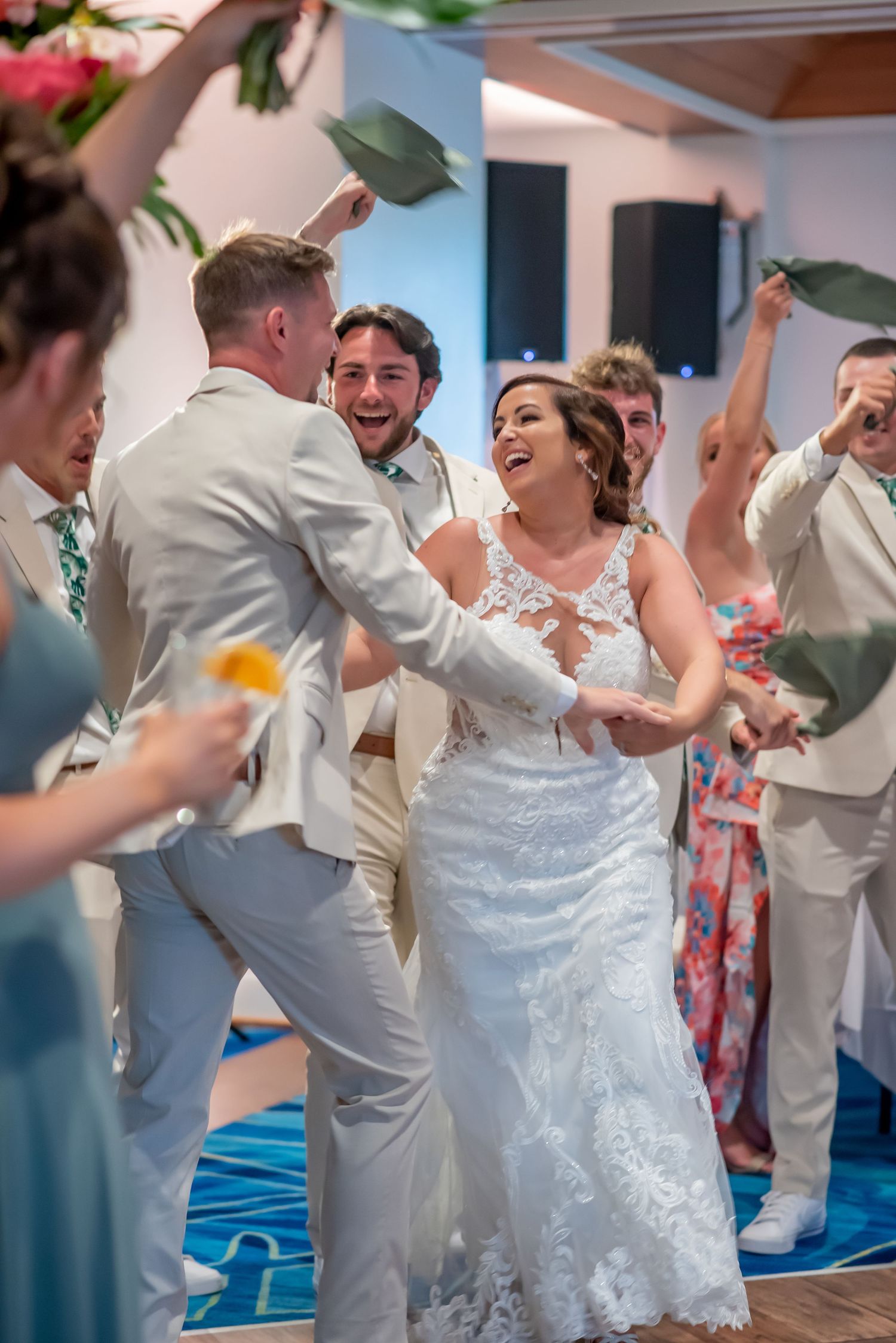 Bride and groom dancing joyfully with wedding party guests in elegant attire at a festive indoor wedding reception.