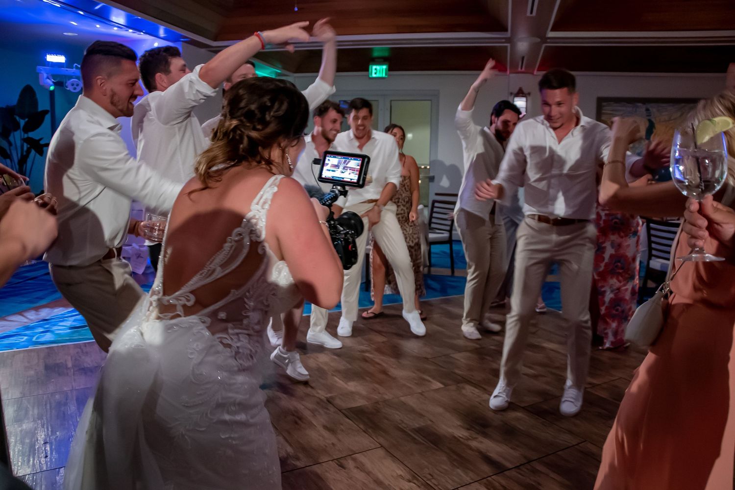 Bride and groom dancing energetically with guests at a lively indoor wedding reception celebration.