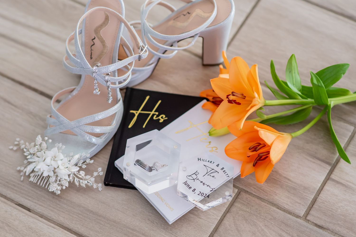 Wedding flat lay with white strappy heels, orange lily, hair comb, and groom gift box.