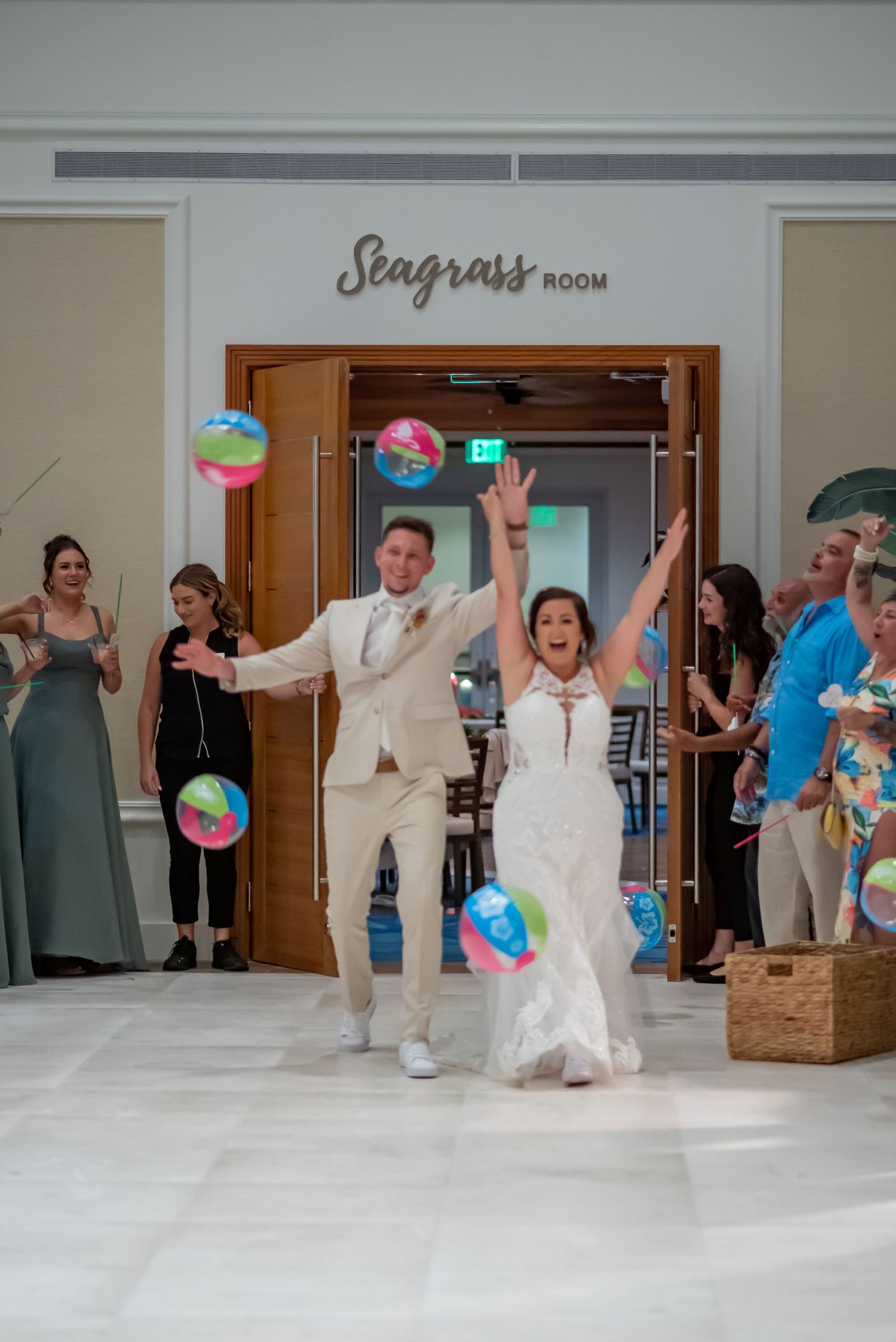 Bride and groom make joyful grand entrance into Seagrass Room with colorful beach balls as guests cheer.