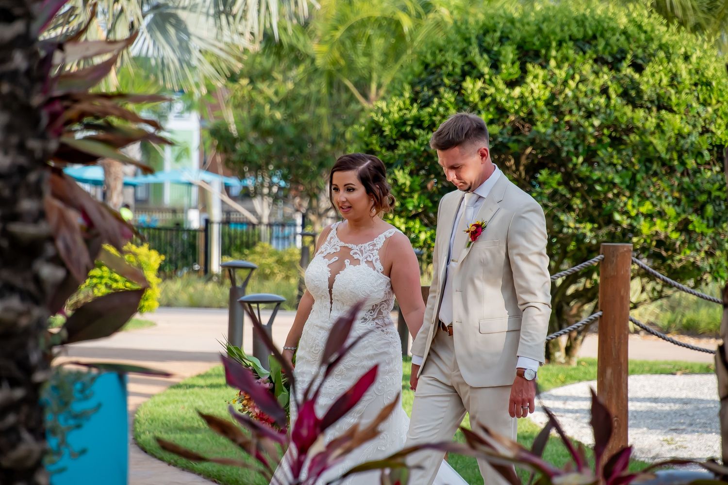 A bride and groom walk hand in hand through a lush tropical garden on their wedding day.