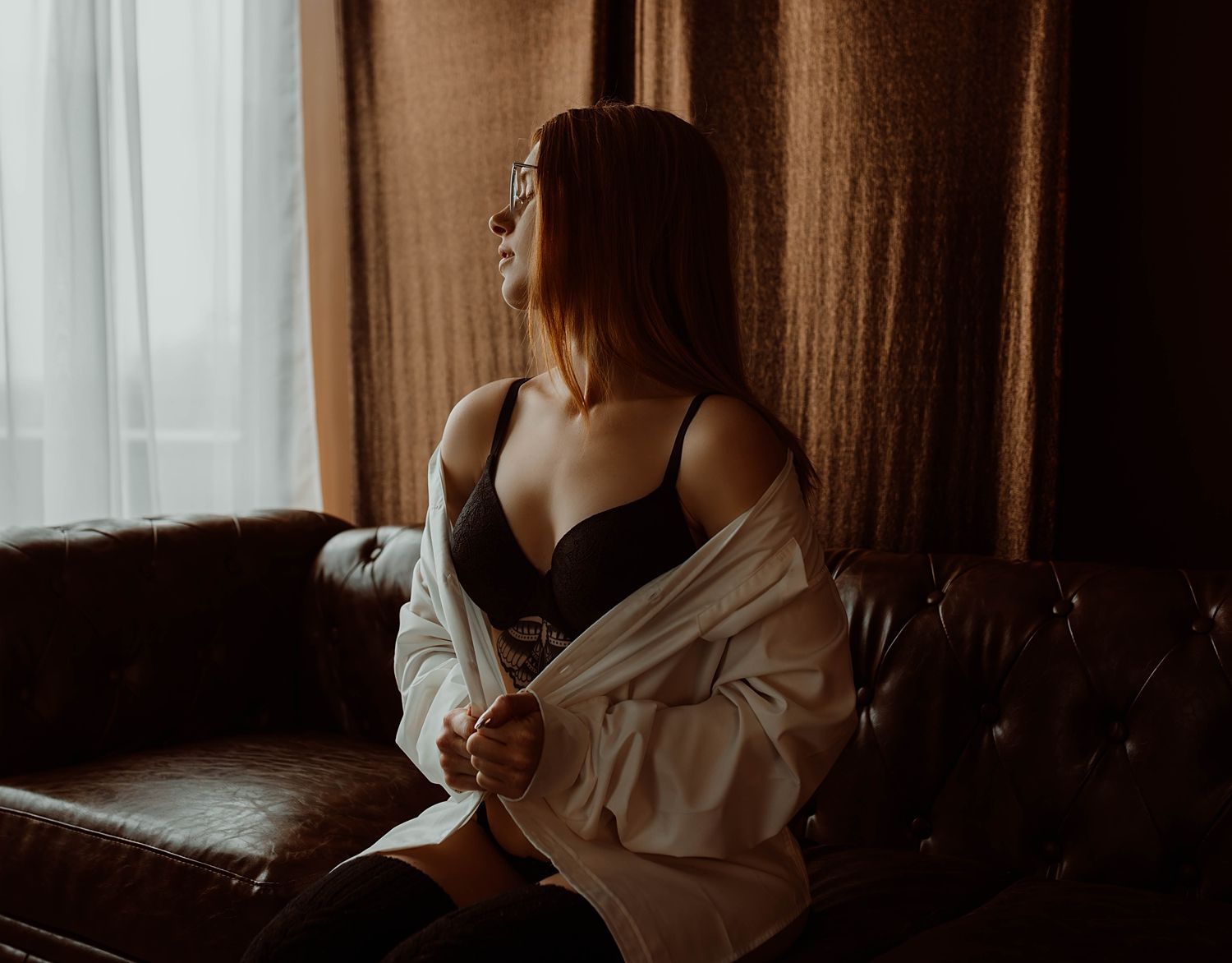 model sits on couch in studio near window by Wisconsin boudoir photographer