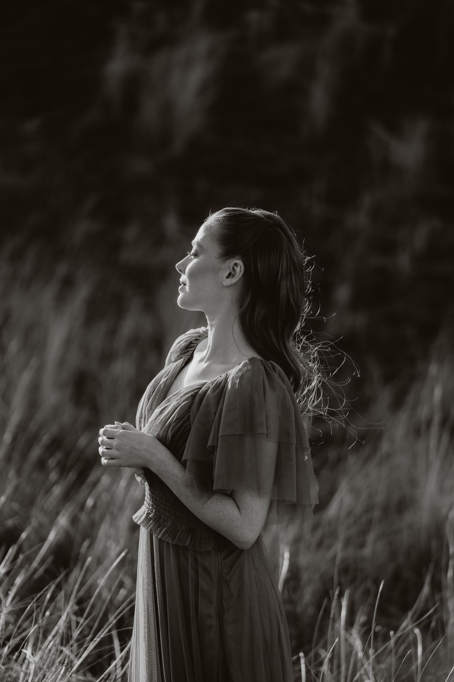Woman in flowing green dress standing in golden sunlit field with rolling hills at sunset.
