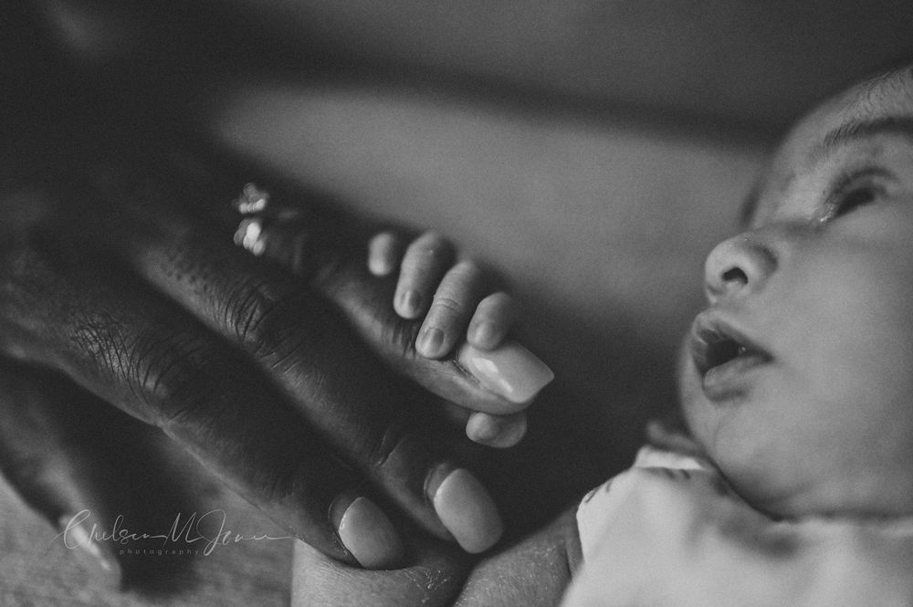 Black and white photo of a newborn baby gently holding an adult finger, capturing a tender moment of new life.