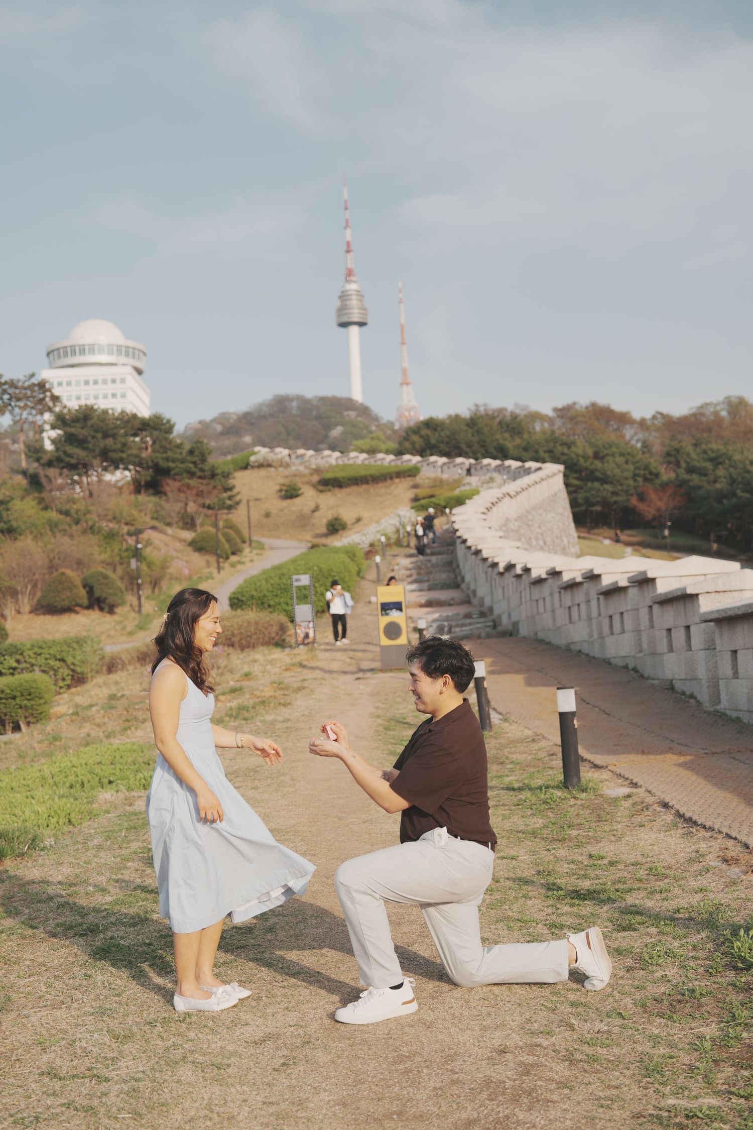 Couple sharing a romantic kiss near Seoul city wall with N Seoul Tower in the background on a sunny day.