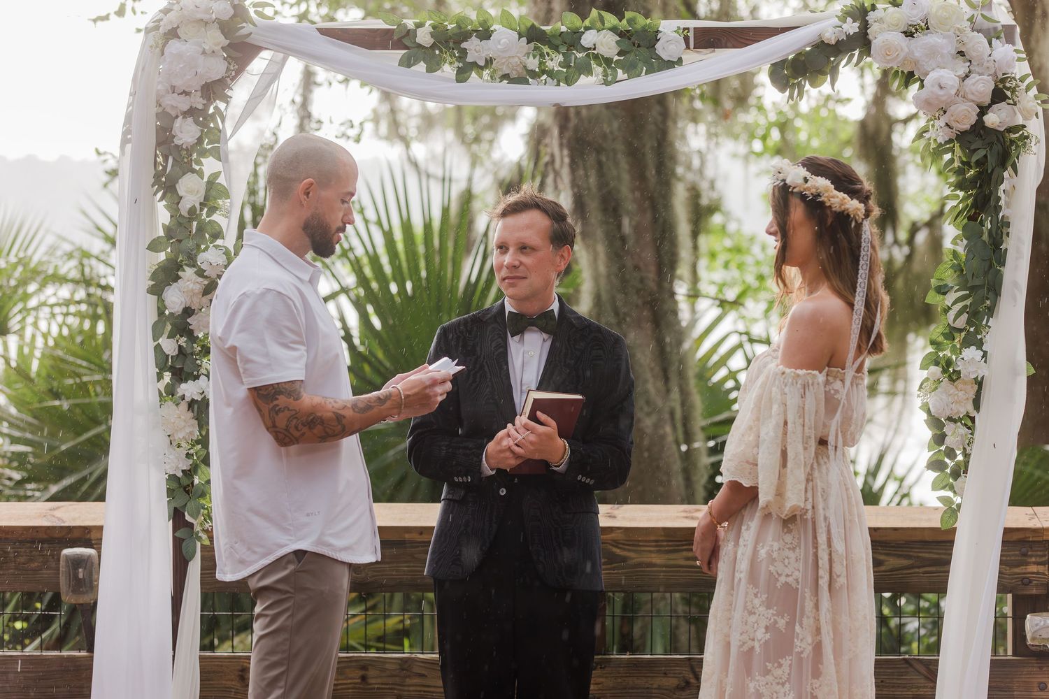 Couple exchanging vows outdoors under floral arch with officiant at elegant garden wedding ceremony.