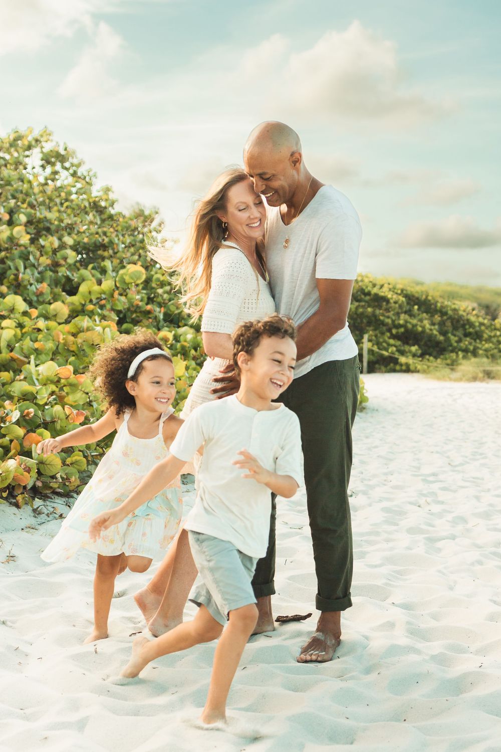 beautiful family photo at the beach with parents standing and children running around them