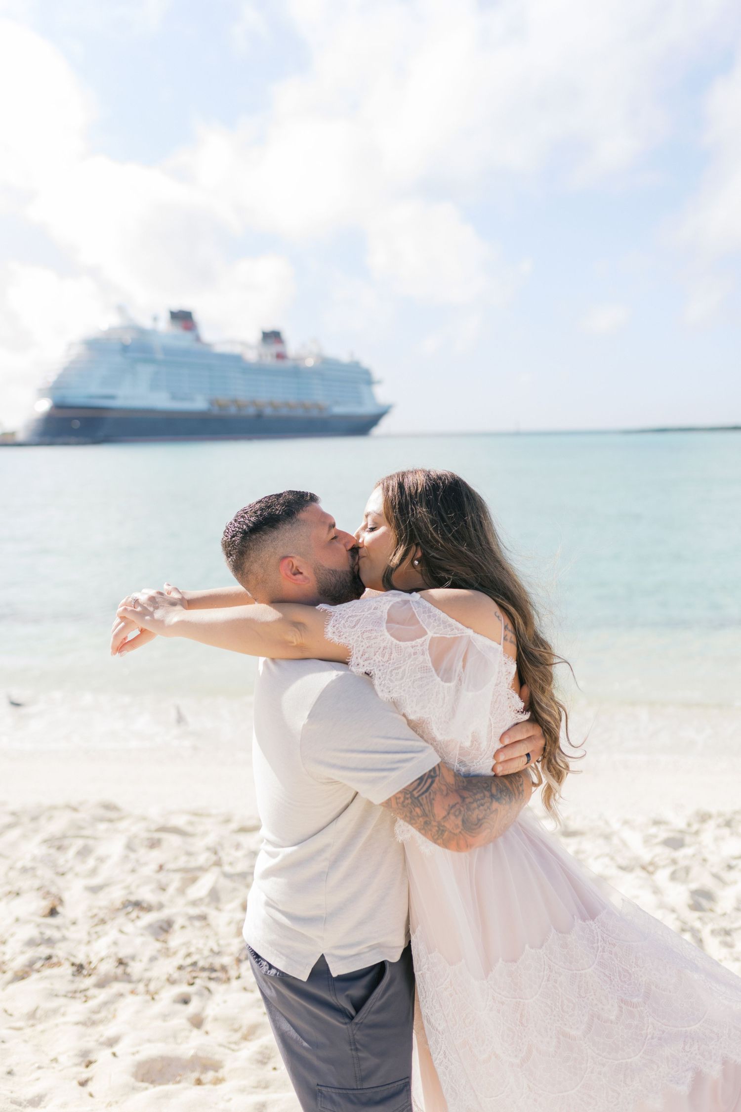 Couple kissing on a tropical beach in wedding attire with a Disney cruise ship in the background.