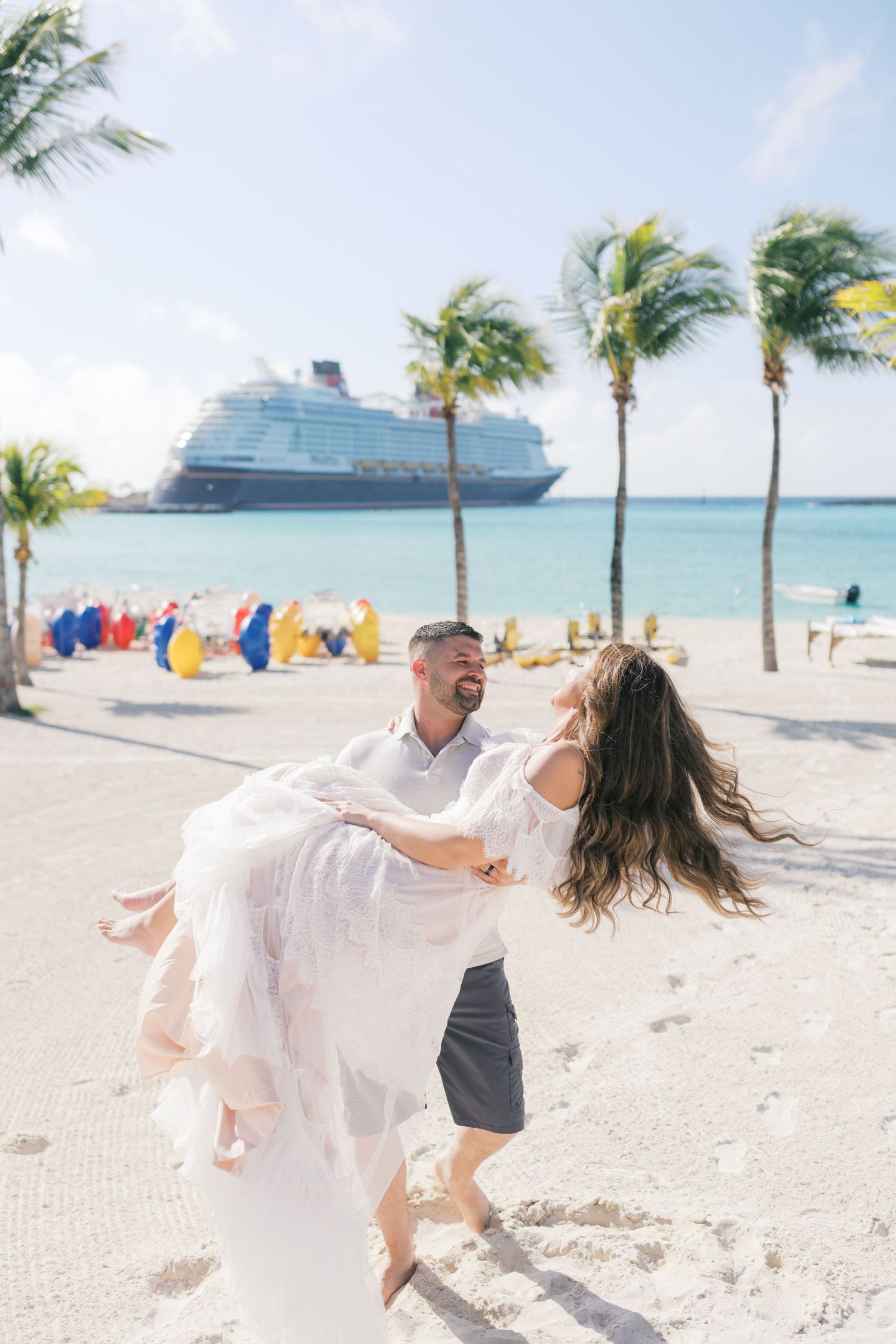 Couple dancing on a tropical beach with palm trees and a cruise ship in the background on a sunny day.