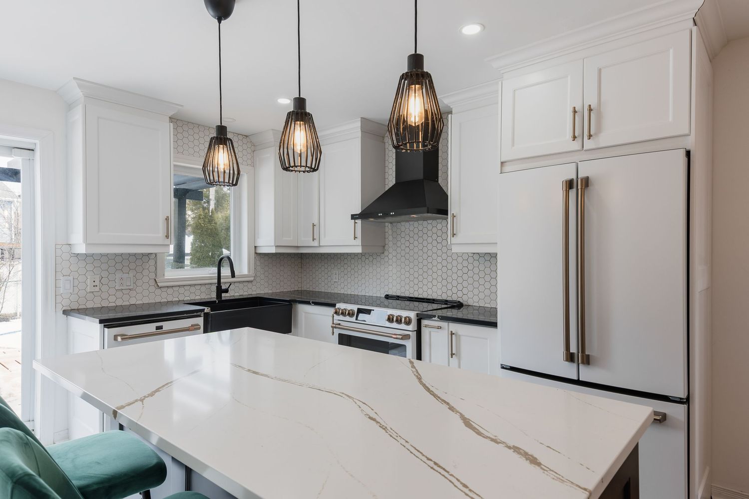 Modern white kitchen with quartz waterfall island, pendant lights, stainless appliances, and subway tile backsplash.