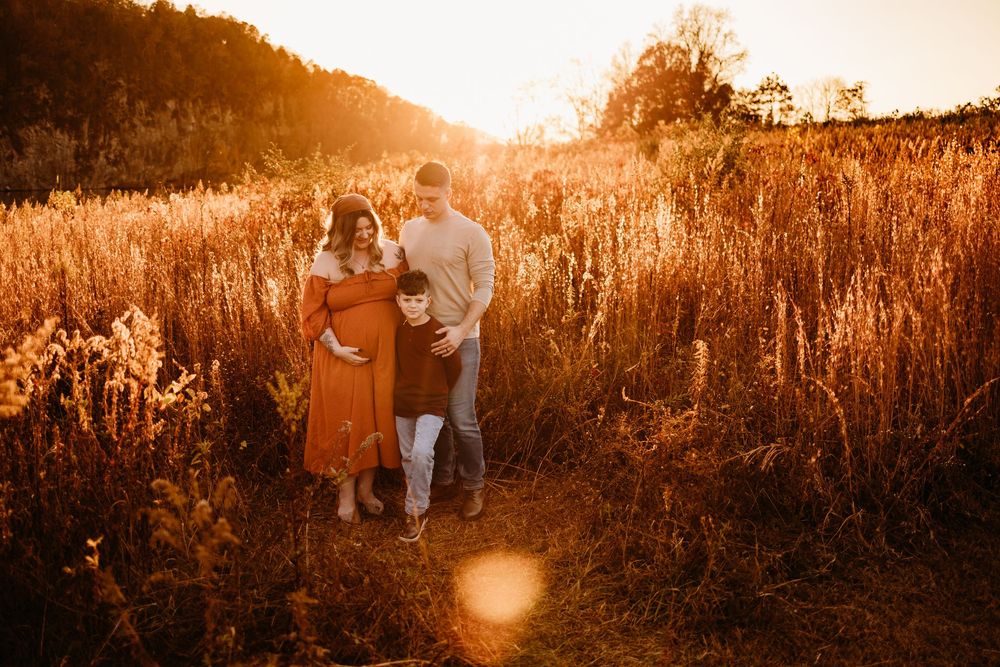 Couple embracing in golden field at sunset during maternity photo session.