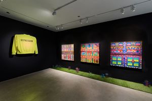 Art gallery installation with neon yellow Depression sweatshirt and colorful grid paintings on dark walls with artificial grass.