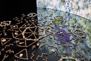 Intricate geometric patterns made from pebbles and stones arranged on a dark floor near a colorful projected wall display.