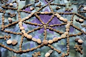 Intricate mandala pattern made from natural river stones arranged on colorful purple and green fabric.