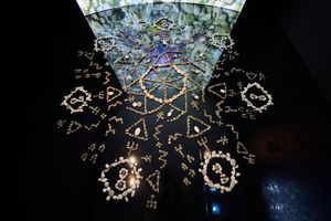 Intricate glowing geometric mandala installation with runic symbols on dark ceiling, illuminated art exhibit.