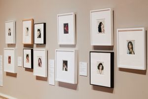 Gallery wall displaying multiple white and black framed portrait photographs of women in a museum exhibition.