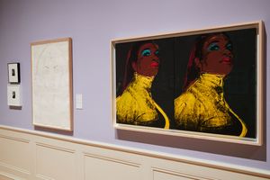 Two Andy Warhol artworks displayed on a lavender gallery wall, including a bold yellow and red double portrait painting.