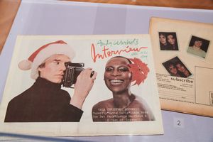 Andy Warhol Interview magazine Christmas issue cover featuring a photographer and smiling woman, displayed with Polaroid photos.