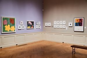 Art gallery wall displaying colorful Andy Warhol prints including flowers and portraits on purple and white walls with parquet floors.