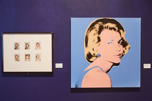 Andy Warhol pop art portrait of Grace Kelly displayed in blue and pink tones beside a framed grid of smaller photographs in a gallery.
