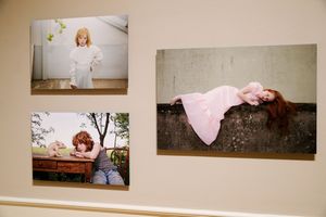 Three fine art photographs displayed on a gallery wall featuring women in pink and white dresses in artistic poses.
