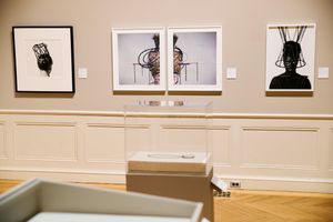 Gallery wall displaying three abstract artworks featuring dark figure silhouettes and colorful wire sculptures in white frames.