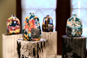 Colorful ceramic vases displayed on rustic wooden stumps in a gallery setting.