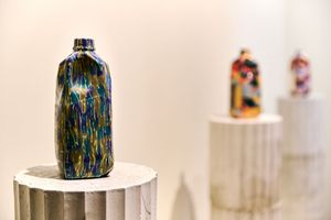 Colorful glazed ceramic bottles displayed on marble pedestals in a gallery setting.