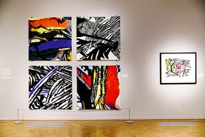 Four bold abstract paintings in black, red, and blue hang in a gallery beside a framed colorful artwork on a white wall.