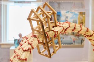 Intricate art installation featuring matchsticks arranged into house-shaped frames along a bundled matchstick serpentine form.