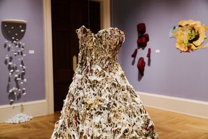 A stunning art installation featuring a dress made of dried leaves on a mannequin displayed in a gallery.