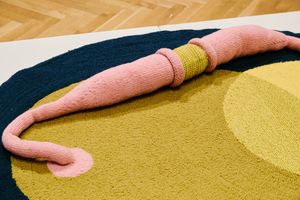 Abstract rug with pink snake sculpture, navy and olive yellow circles on wooden floor.