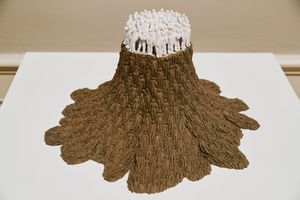 Sculptural artwork resembling a volcano with brown textured base and white clustered top, displayed on a white pedestal.