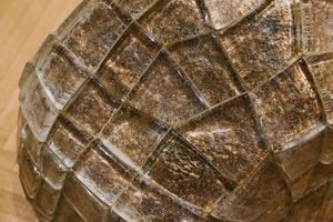 Close-up detail of a large sculptural artwork with dark brown cracked and gridded textured surface resembling stone or resin.