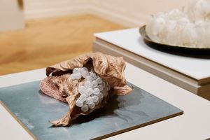 Sculptural art piece featuring dried organic material and translucent glass beads on a blue ceramic tile in a gallery.