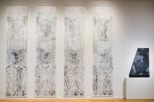 Four large ornate botanical panel drawings displayed on a white gallery wall beside a small dark abstract artwork on a pedestal.