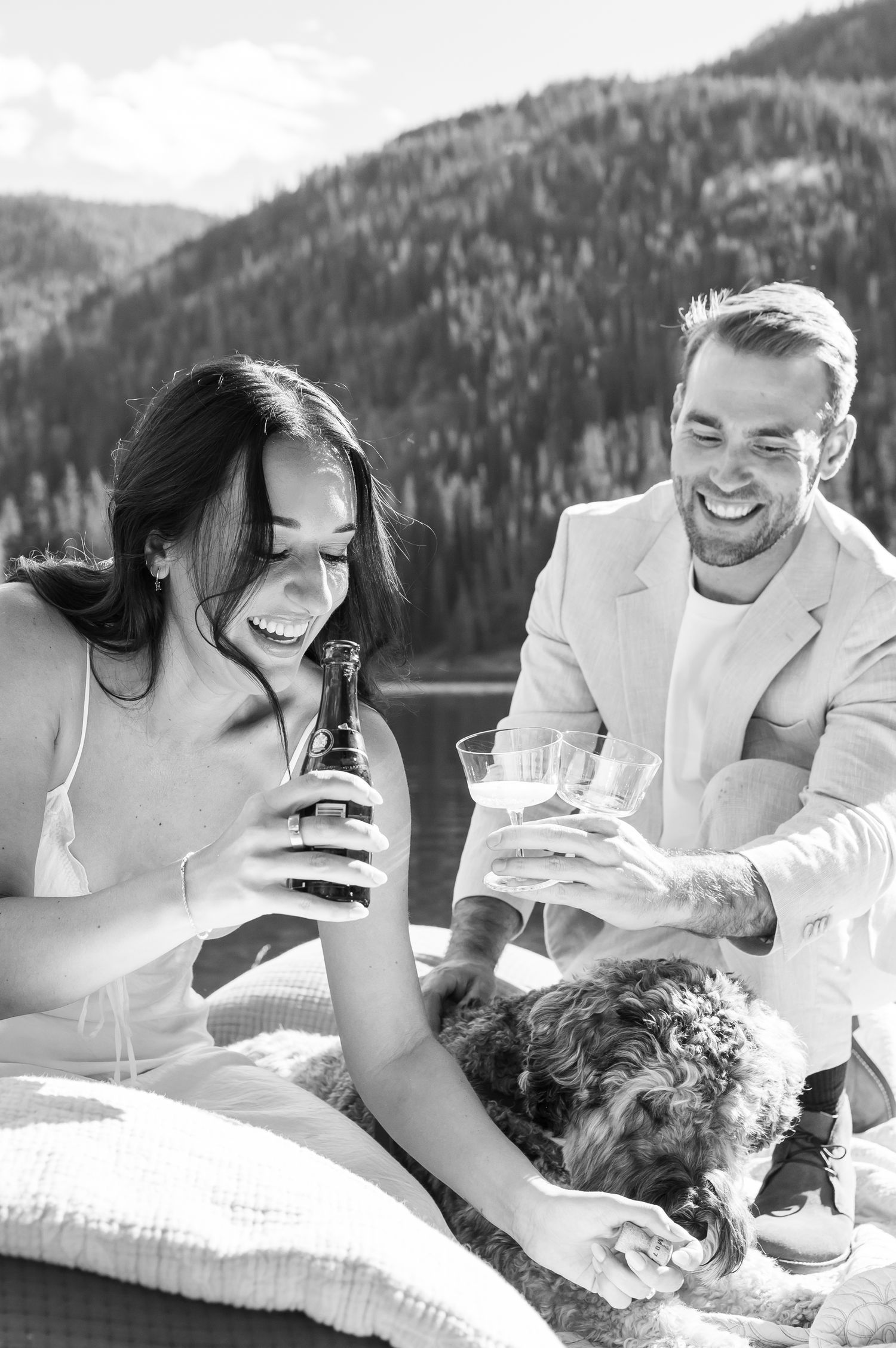 Black and white photo of a laughing couple enjoying drinks outdoors with their dog for a spring elopement at Officer's Gulch